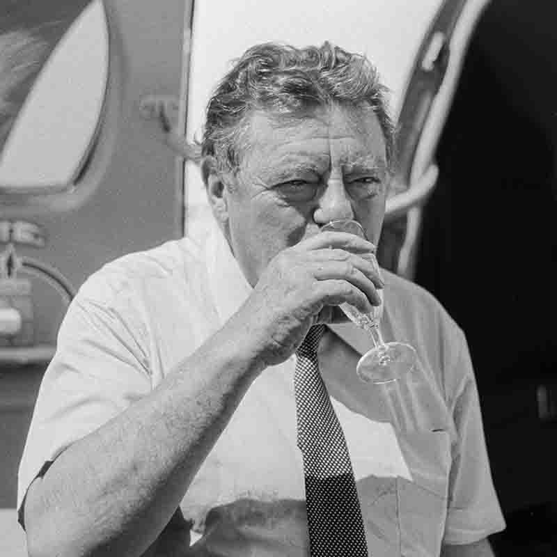 Franz Josef Strauß trinkt aus einem Sektglas vor einem Flugzeug, Schwarz-Weiß-Fotografie von Ingeborg Bock-Schroeder.
