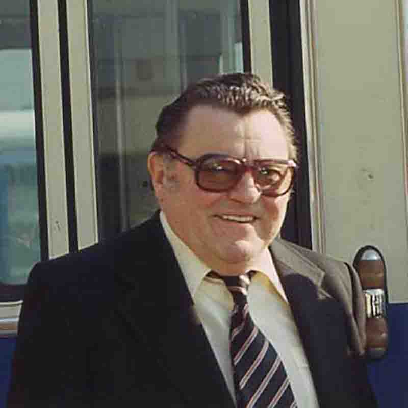 Porträtaufnahme von Franz Josef Strauß in München. Der bayerische Ministerpräsident trägt eine markante Brille, einen dunklen Anzug und eine gestreifte Krawatte vor dem Hintergrund einer Strassenbahn.