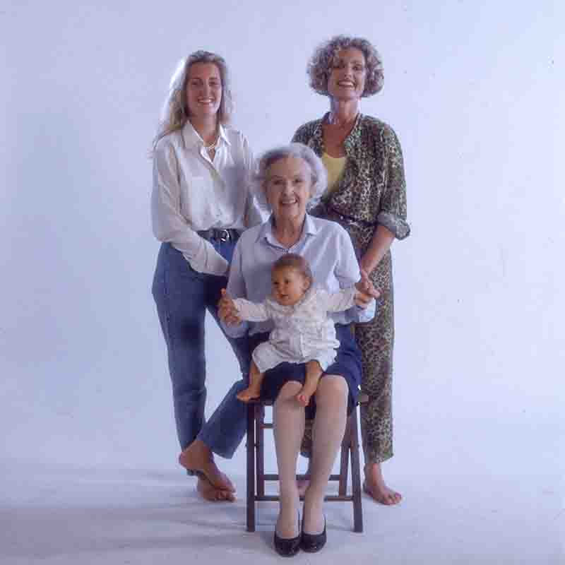 Vier Generationen der Furtwängler Familie: Grossmutter Elisabeth Furtwängler sitzt mit ihrer Enklin Elisabeth Furtwängler auf dem Schoß auf einem Stuhl, flankiert von den lächelnden Maria Furtwängler und Katrin Ackerman vor hellem Studion Hintergrund.
