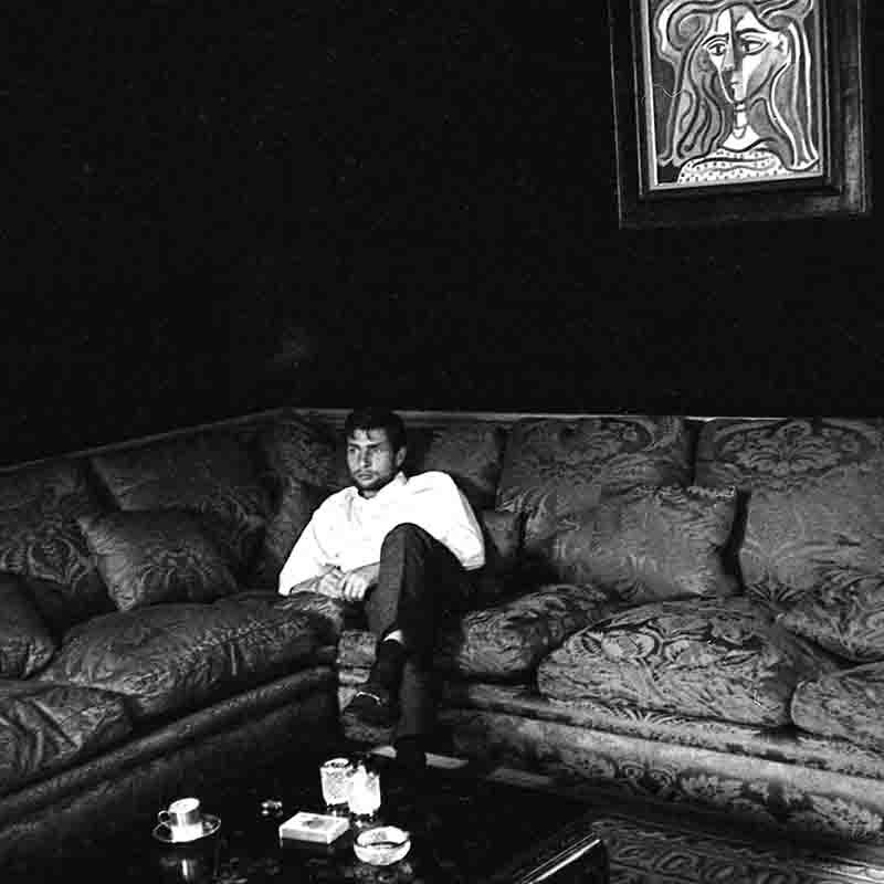 Eine Schwarz-Weiß-Fotografie von Gunter Sachs, der auf einem Ecksofa mit Brokatbezug sitzt und sinniert. Über ihm an der dunklen Wand hängt das gerahmtes kubistische „Buste de femme“ von Pablo Picasso. Ein Couchtisch mit einem Aschenbecher und Gläsern steht im Vordergrund.