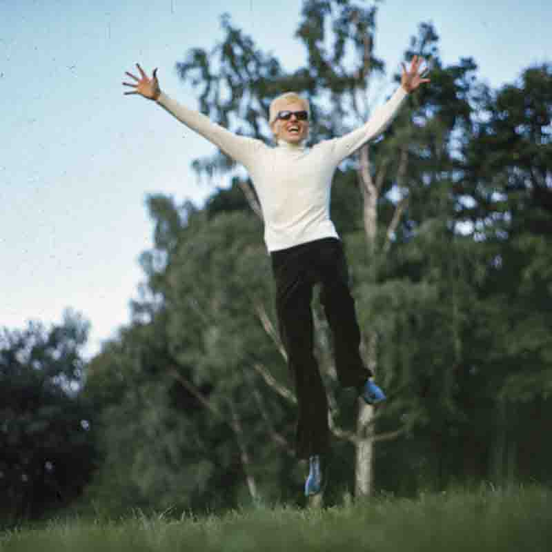 Porträt des Sängers Heino, der mit ausgebreiteten Armen jubelnd in die Luft springt, vor einer Waldkulisse. Foto von Ingeborg Bock-Schroeder.