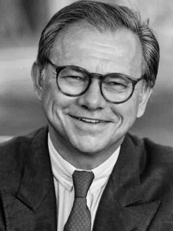 Schwarz-Weiß-Porträt von Hubert Burda mit Brille, Anzug und Krawatte, lächelnd in die Kamera blickend.