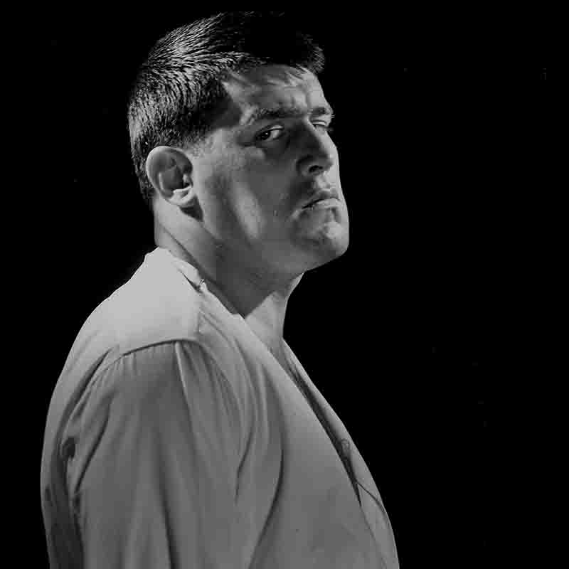 Schwarz-Weiß-Portrait Mario Adorfs, fotografiert von Ingeborg Bock-Schroeder. Der Charakterdarsteller blickt direkt in die Kamera, markantes Gesicht, ausdrucksstarke Augen — ein Bild, das seine intensive Bühnenpräsenz einfängt.